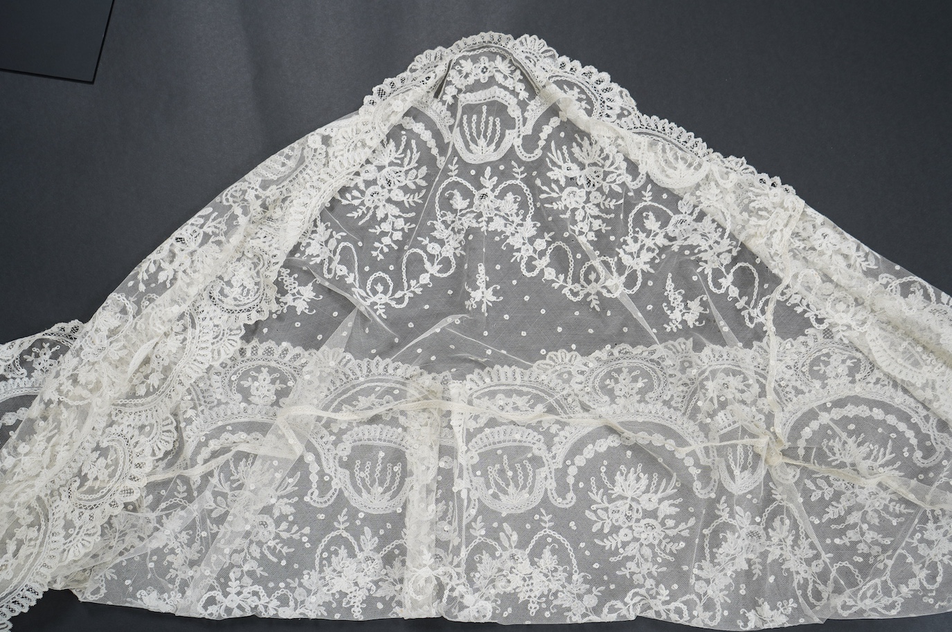 A wide flounce of fine ornate hand made 19th century Brussels bobbin lace, appliquéd onto a net ground, possibly commissioned for a wedding gown, now sewn together along the top edge and the two cut ends also stitched to